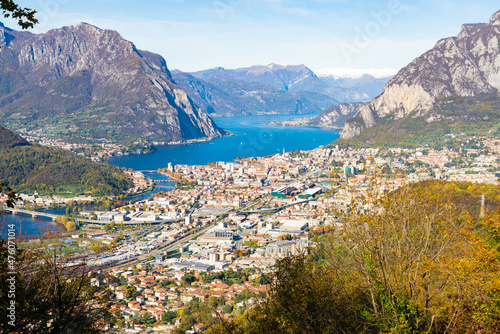 Aerial view of the city of Lecco  Italy  with the blue waters of Lake Como. Italian alps with blue sky on the background. Bushes on the foreground 