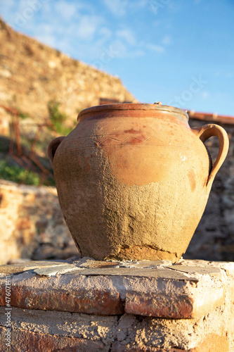 An antique earthenware jug with handles stands on brickwork outside against the backdrop of a rustic landscape. Spain.