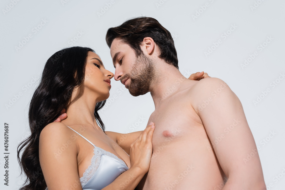 brunette woman in satin bra and shirtless man standing to face while hugging isolated on grey. brunette woman in satin bra and shirtless man standing to face while hugging isolated on grey.