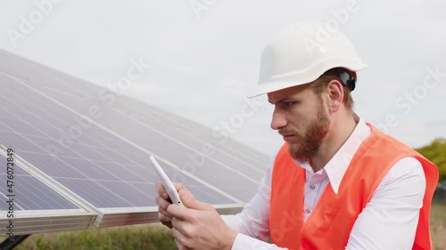 In front of the camera at new modern solar power station ecological engineer using digital tablet to controlling the photovoltaic batteries from wireless hew wearing safety helmet