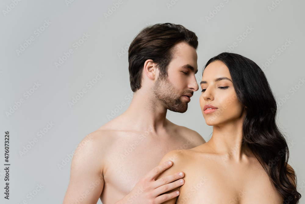 young shirtless man touching nude brunette woman isolated on grey. young shirtless man touching nude brunette woman isolated on grey.