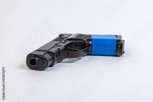 Black pistol with a handle wrapped in blue electrical tape on a white background