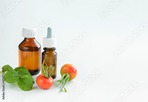 Concept alternative medicine. Two medical dark bottles and rose hip fruits with green leaves on white background. Copy space