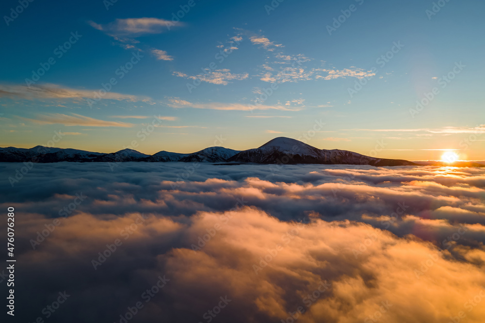 Aerial view of vibrant sunrise over white dense clouds with distant dark mountains on horizon