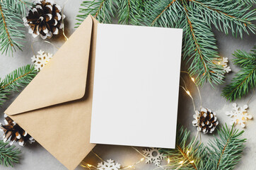 Christmas or New Year greeting card mockup with envelope, fir tree branches with cones and lighting garlands