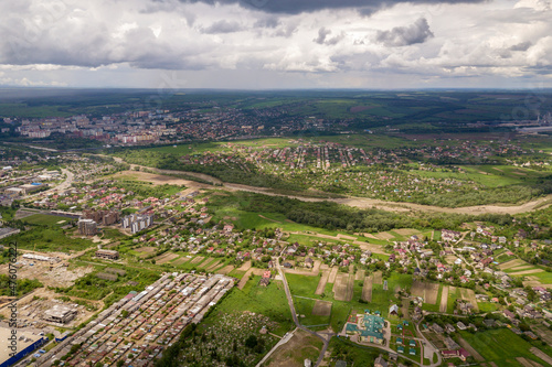 Aerial view of town or village with rows of buildings and curvy streets between green fields in summer. Countryside landscape from above. © bilanol
