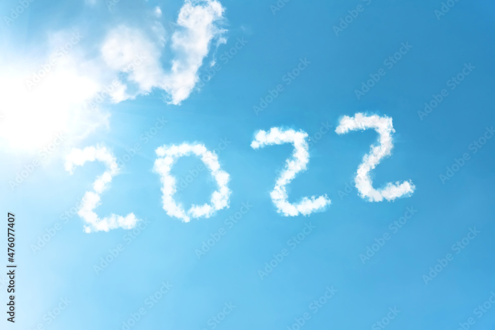 Numbers 2022 symbol inscription on a background of blue sky from white smoke of clouds lit by a bright sun.