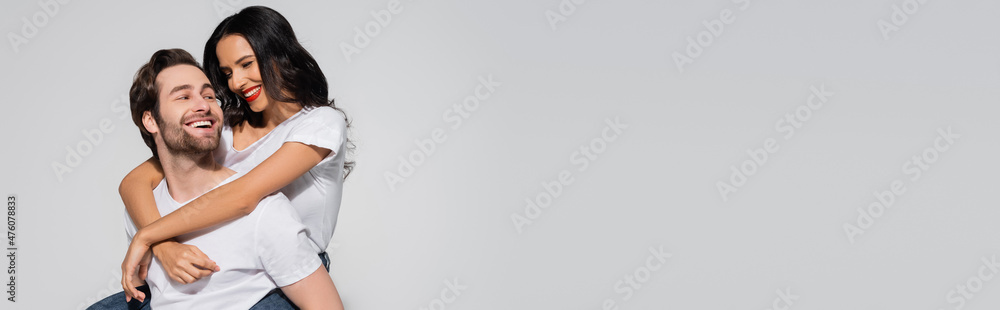 cheerful man piggybacking young brunette woman isolated on grey, banner. cheerful man piggybacking young brunette woman isolated on grey, banner.