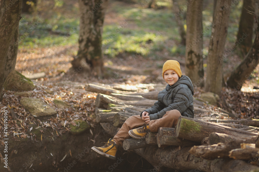 A cute blond boy in the spring forest is sitting on the bridge of the river. The boy looks into the frame. The concept of life after quarantine. High-quality photography A cute blond boy in the spring forest is sitting on the bridge of the river. The boy looks into the frame. The concept of life after quarantine. High-quality photography