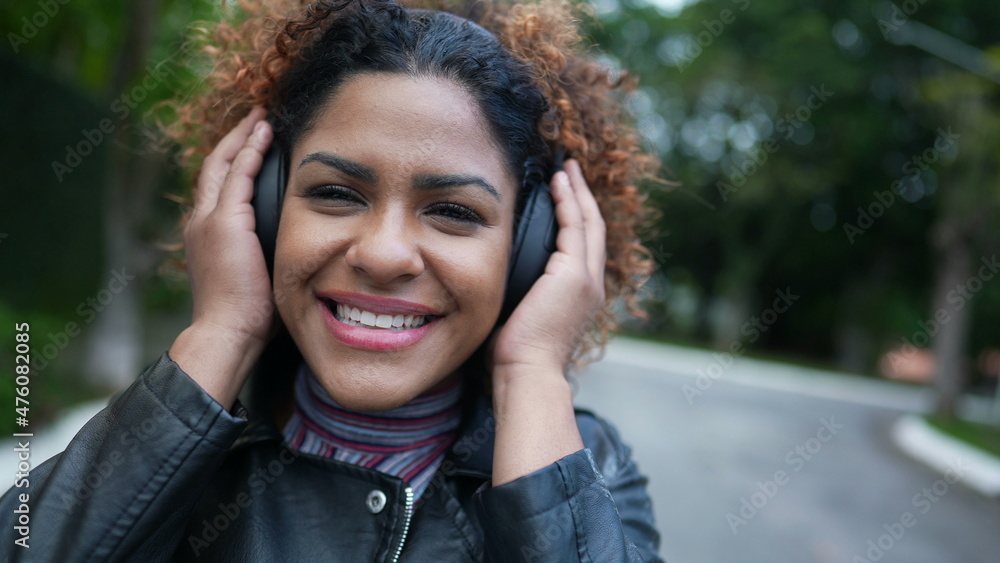 Happy Brazilian woman listening to music wearing headphone in street