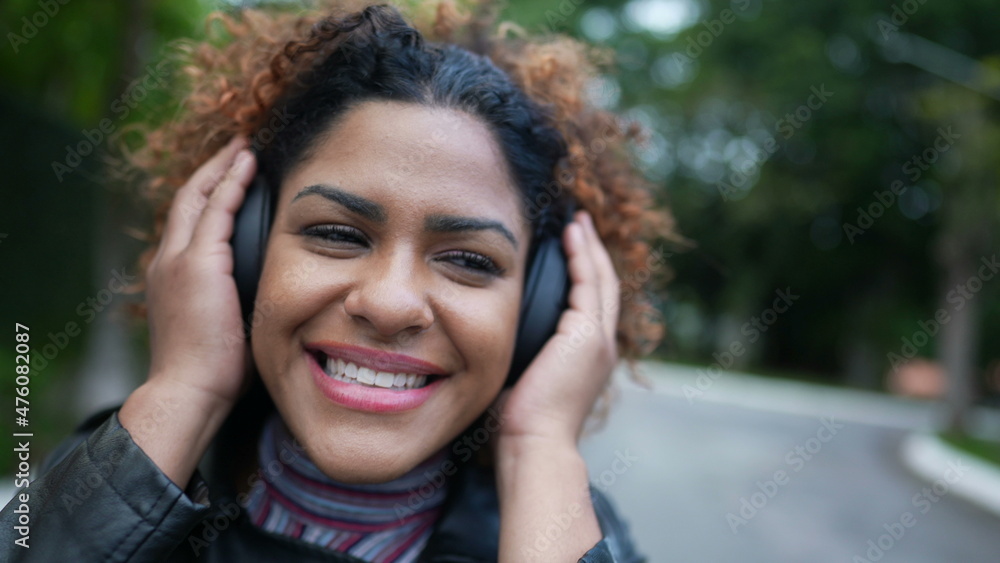 Happy Brazilian woman listening to music wearing headphone in street