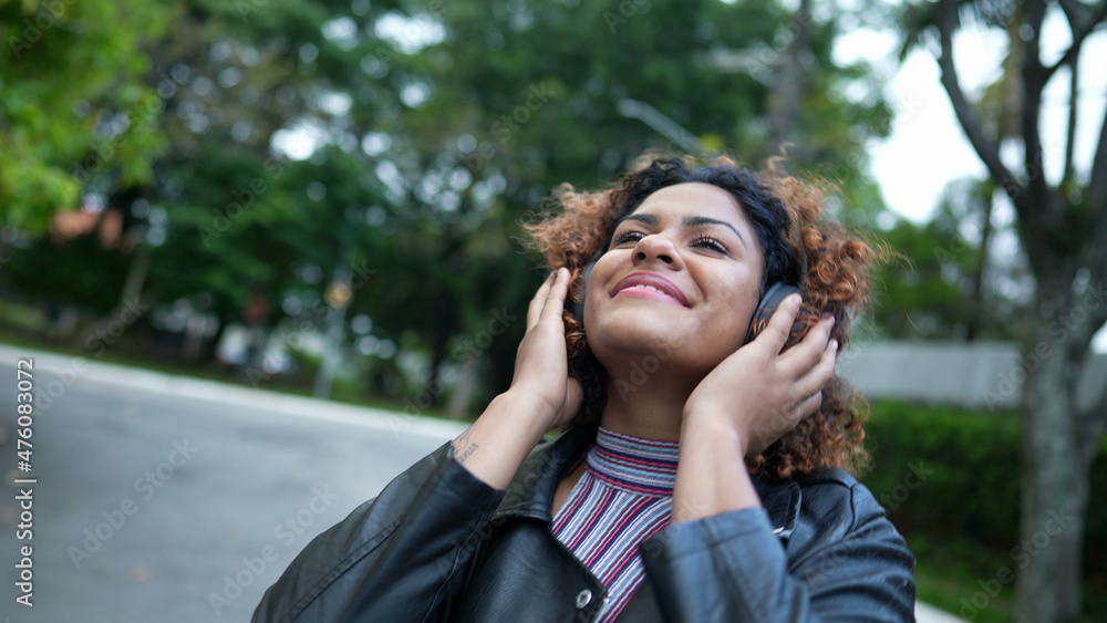 Carefree black woman dancing to music outside in street wearing headphones