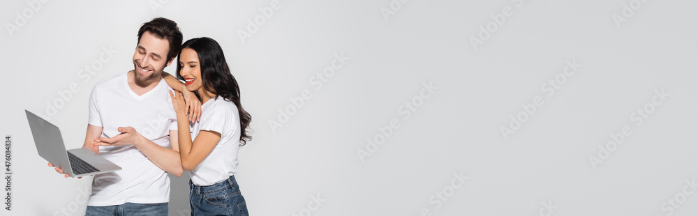 cheerful man in white t-shirt pointing at laptop near smiling girlfriend on grey, banner. cheerful man in white t-shirt pointing at laptop near smiling girlfriend on grey, banner.