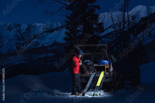 Man with splitboards standing by truck in snow