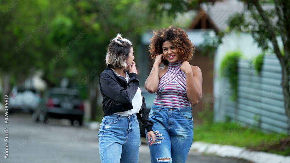 Candid two diverse women walking together outside in street laughing and smiling