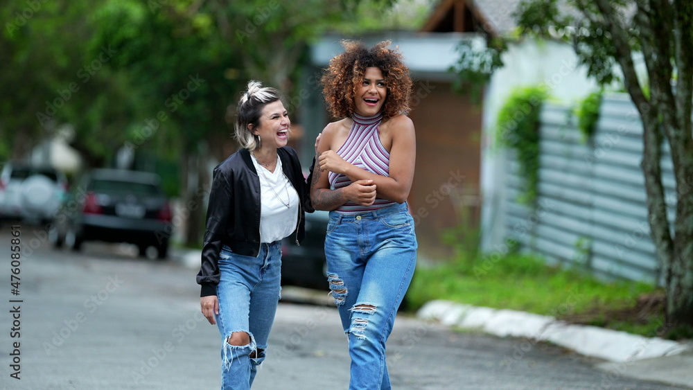 Candid two diverse women walking together outside in street laughing and smiling Candid two diverse women walking together outside in street laughing and smiling