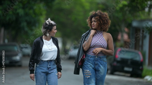 Candid two diverse women walking together outside in street laughing and smiling