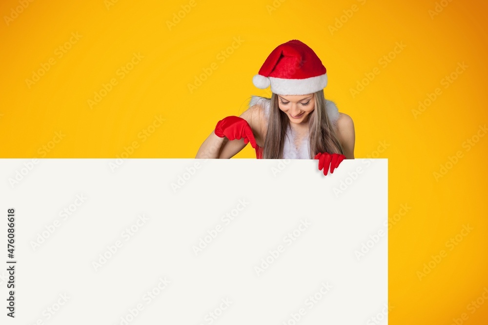 Christmas Happy woman In Santa Hat Pointing At White Advertisement Board With Hand. Christmas Happy woman In Santa Hat Pointing At White Advertisement Board With Hand.