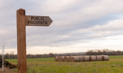 Public footpath sign with blurred hay bales behind, rural walk in the UK countryside