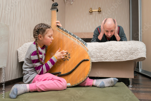 The child loudly plays the bandura, and dad lies on the bed with his hands over his ears. A girl with loud music interferes with a man's rest