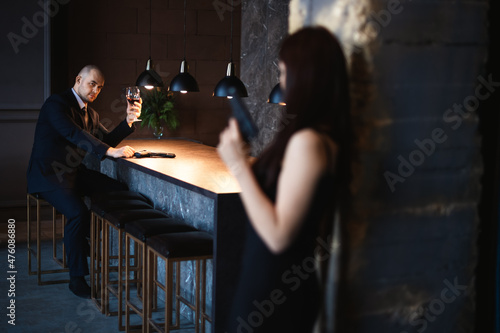 Man and woman, stills from the film. Bald man sits in a bar with a glass of wine and a gun, brunette girl with a gun looking at him