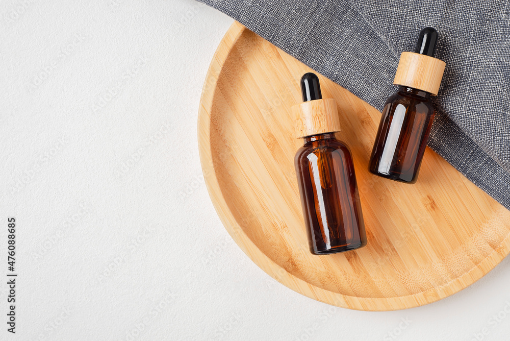 Amber glass dropper bottles with bamboo lid on wooden plate for product presentation. Skincare cosmetic on grey fabric. Beauty concept for face body care
