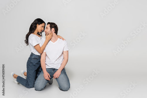 full length view of passionate woman touching face of young man while standing on knees on grey background.