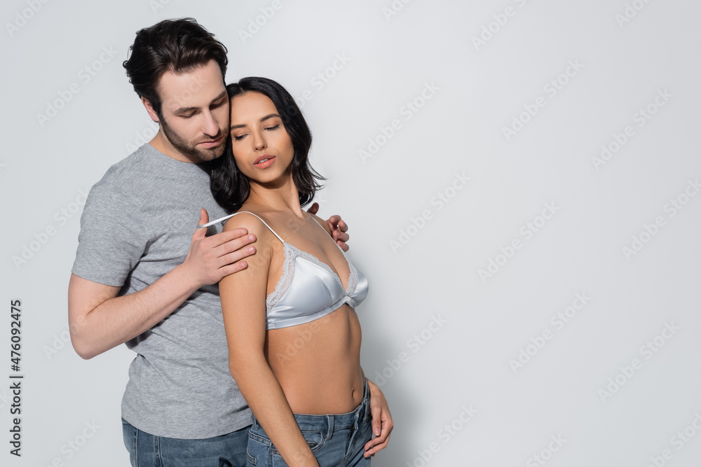 Naklejka premium man in t-shirt touching satin bra of young passionate woman on grey.