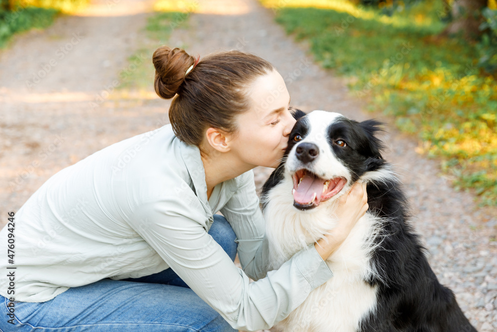 Smiling young attractive woman playing with cute puppy dog border collie on summer outdoor background. Girl holding embracing hugging dog friend. Pet care and animals concept Smiling young attractive woman playing with cute puppy dog border collie on summer outdoor background. Girl holding embracing hugging dog friend. Pet care and animals concept