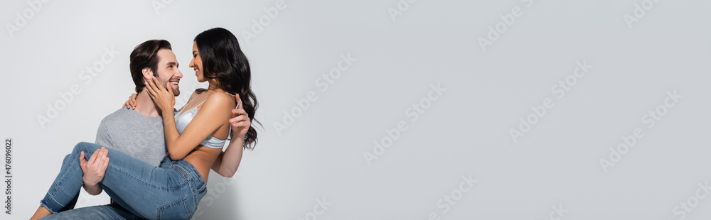 smiling man holding sexy woman in jeans and bra embracing him on grey, banner. smiling man holding sexy woman in jeans and bra embracing him on grey, banner.