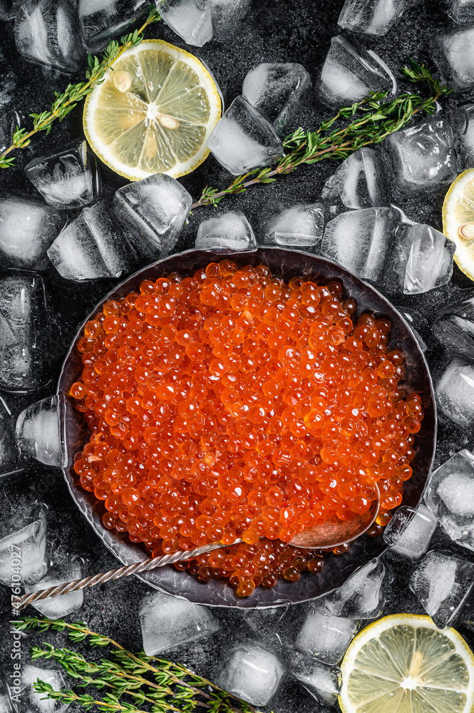 Salty Red caviar in steel plate on ice. Black background. Top view