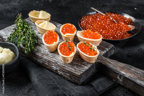 Tartlets with Red caviar, butter and thyme on wooden board. Black background. Top view