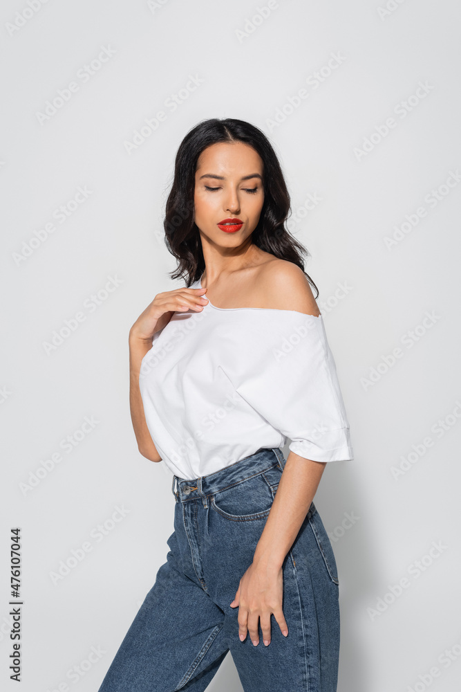 sensual woman with red lips posing in white t-shirt with naked shoulder on grey.