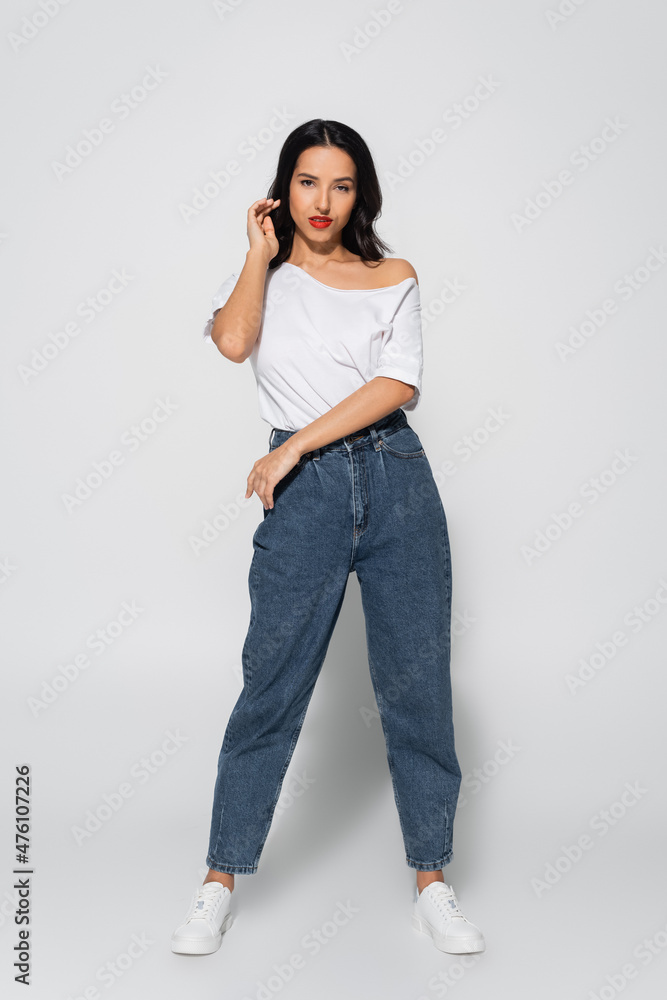 full length view of brunette woman in jeans and white t-shirt posing on grey. full length view of brunette woman in jeans and white t-shirt posing on grey.