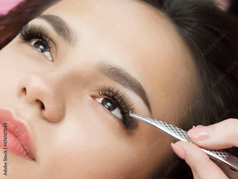 Eyelash extensions. a young woman undergoes a close-up eyelash extension procedure. Tweezers.