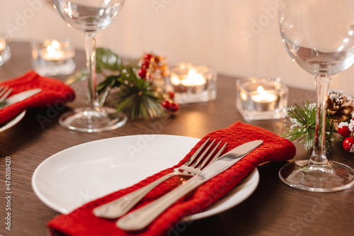 Christmas table setting. Plate and cutlery on napkin. Preparing for festive dinner. Candles burning on table on Christmas Eve.