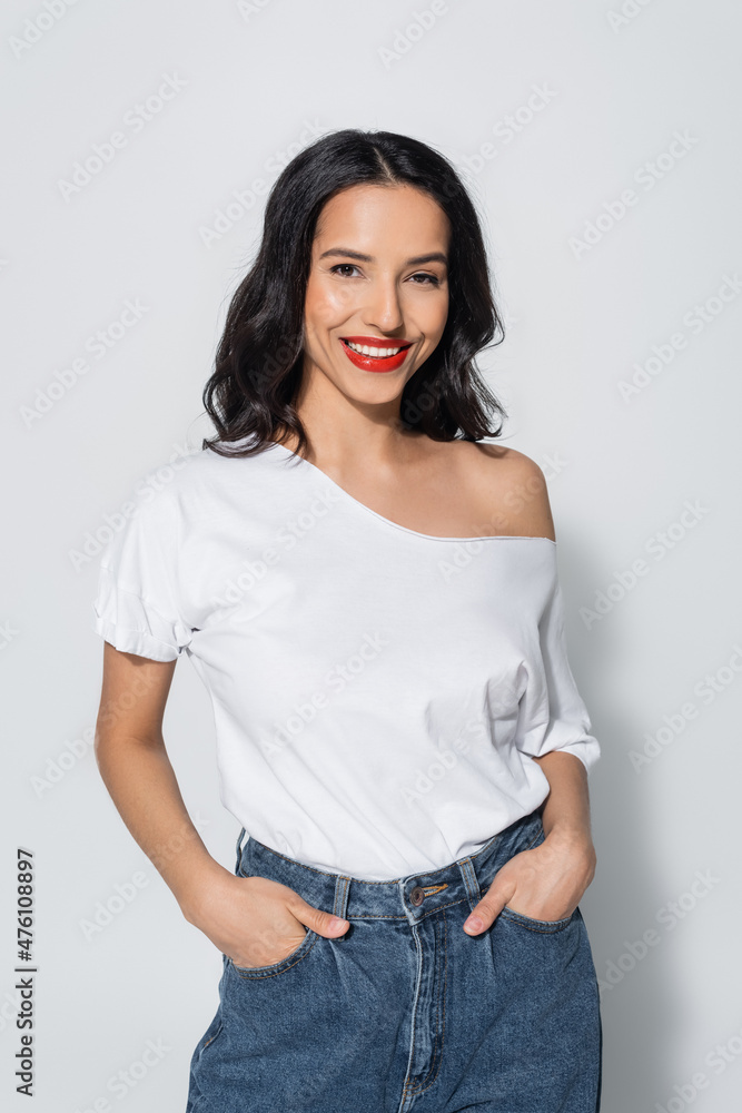 happy woman with red lips and naked shoulder posing with hands in pockets of jeans on grey. happy woman with red lips and naked shoulder posing with hands in pockets of jeans on grey.