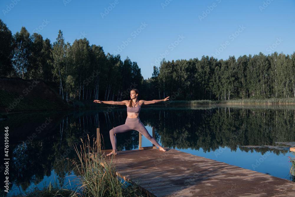 Young woman on wooden pier above forest lake scenery, folds her arms in a namaste gesture. Woman arms outstretched in nature.