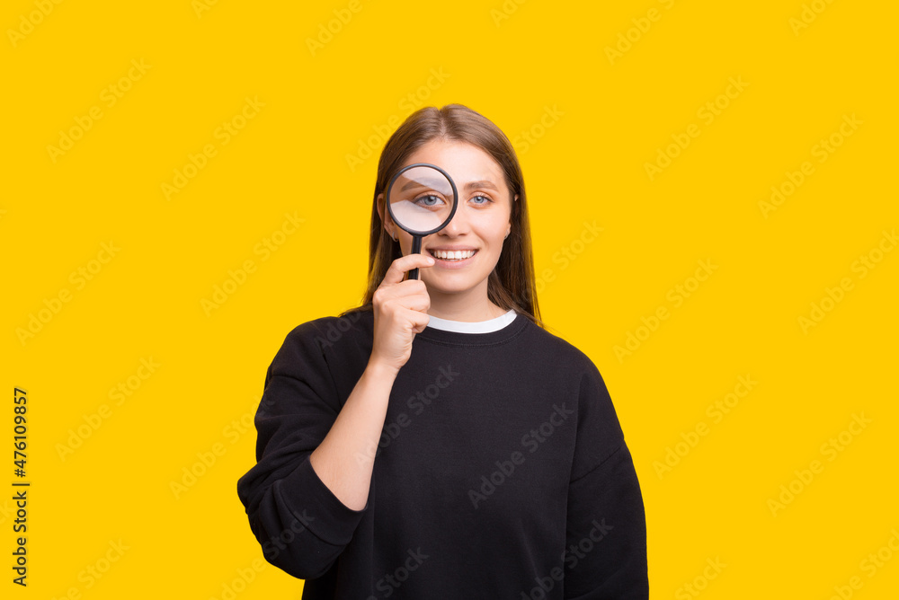 Portrait of cheerful pretty woman looking at camera through magnifying glass, isolated over yellow background Portrait of cheerful pretty woman looking at camera through magnifying glass, isolated over yellow background
