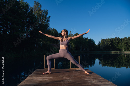 Young woman on wooden pier above forest lake scenery  folds her arms in a namaste gesture. Woman arms outstretched in nature.