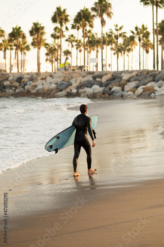 Canvas Print View of a man with a surfing board on the beach with palms trees at sunset