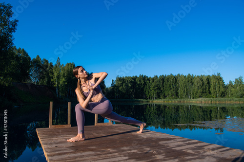 Young Woman practicing yoga on the wooden berth at lake. Single sport healthy training on nature at sunny weather © romankosolapov