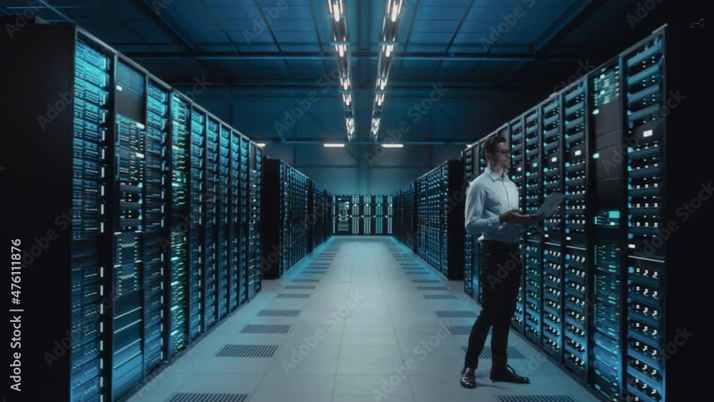 Big Data Center IT Specialist Using Laptop Computer. Server Farm Cloud Computing Facility with System Administrator Working. Software as Solution, Cyber Security. Moving Between Rack Raws Dolly Shot Big Data Center IT Specialist Using Laptop Computer. Server Farm Cloud Computing Facility with System Administrator Working. Software as Solution, Cyber Security. Moving Between Rack Raws Dolly Shot
