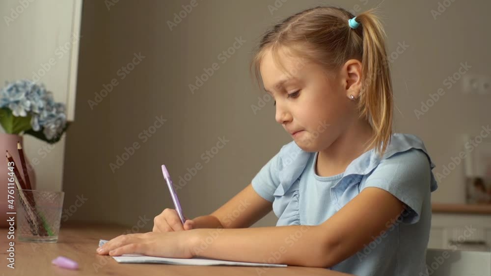 Close-up of thoughtful pretty primary girl child learning writing doing homework sitting at home table by window. Adorable little preschool kid studying alone making note. Shooting in slow motion. Close-up of thoughtful pretty primary girl child learning writing doing homework sitting at home table by window. Adorable little preschool kid studying alone making note. Shooting in slow motion.