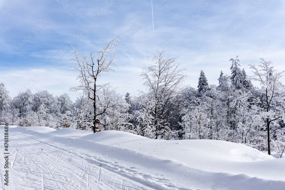 Winter mountain landscape. Trail to cross-country skiing on a mountain road, trees covered with hoarfrost and snow, blue sky with white clouds. Kremnica Mountains, Slovakia. Winter mountain landscape. Trail to cross-country skiing on a mountain road, trees covered with hoarfrost and snow, blue sky with white clouds. Kremnica Mountains, Slovakia.