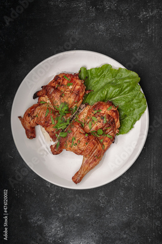 Fried tobacco chicken with a leaf of lettuce on a plate, on a dark background