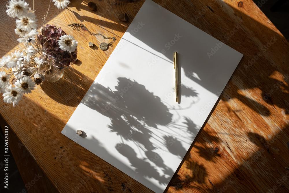 White paper sheet with golden pen on a wooden table with flowers and vintage elements. 