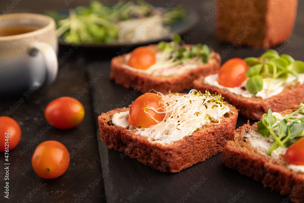 Red beet bread sandwiches with cream cheese, tomatoes and microgreen on black. side view, selective focus. Red beet bread sandwiches with cream cheese, tomatoes and microgreen on black. side view, selective focus.