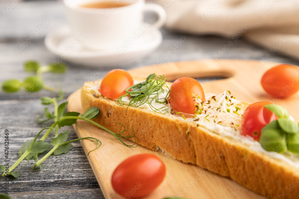 Long white bread sandwich with cream cheese, tomatoes and microgreen on gray. side view, selective focus. Long white bread sandwich with cream cheese, tomatoes and microgreen on gray. side view, selective focus.