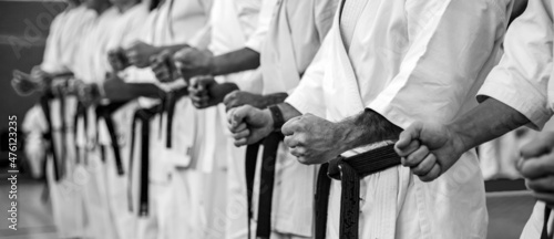 Karate master in a white kimono and with a black belt, stands in front of the formation of his students. Martial arts school in training in the gym.
